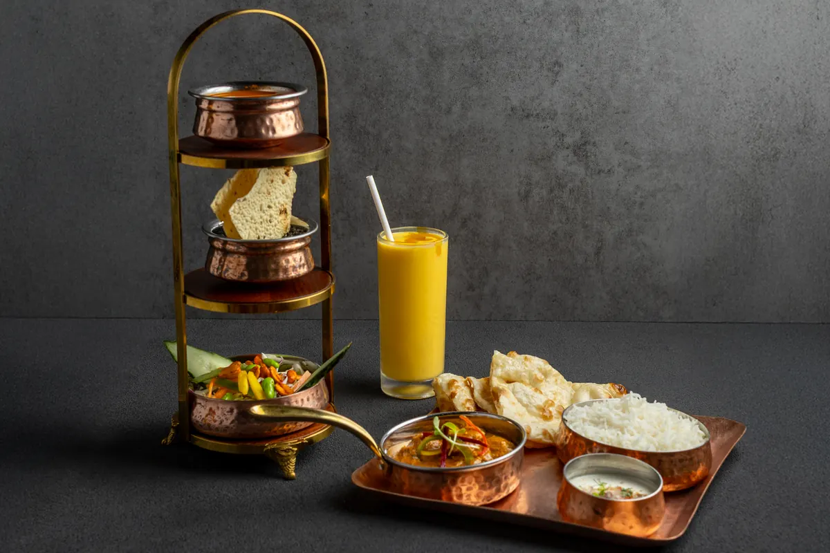 An express set lunch: a copper tiffin tower beside a lunch tray and a mango drink